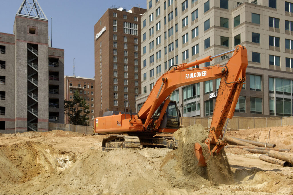 Excavator digging on a construction site in a city surrounded by buildings