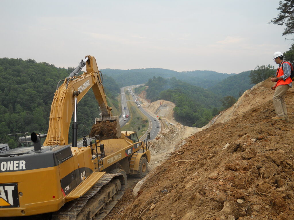 Excavator loading truck with interstate highway in the background