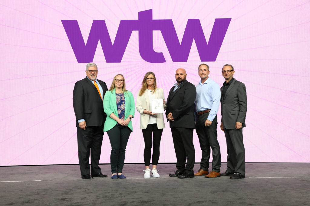Group of people accepting an award in front of a purple backdrop